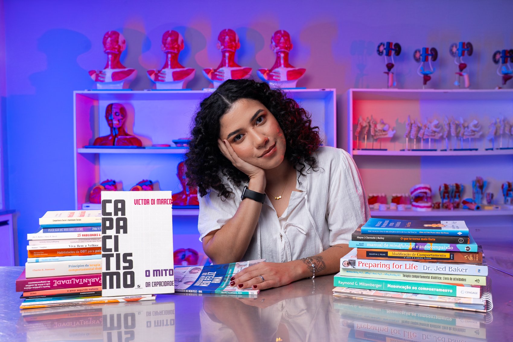 Marinalva Gama apoiada em uma mesa com diversos livros de análise do comportamento